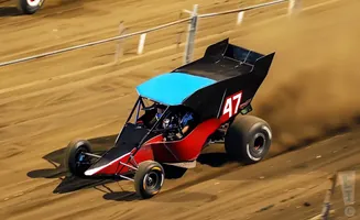 A sprint car with the number 47 races on a dirt track, kicking up dust.