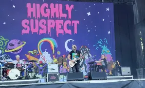 Highly Suspect band performs on stage with a colorful, psychedelic backdrop featuring a starry sky and alien-like creatures.