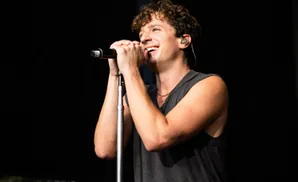 A man with curly hair smiles while singing into a microphone on stage.
