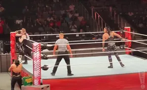 Wrestlers in a ring with a referee, a Money in the Bank briefcase to the side.