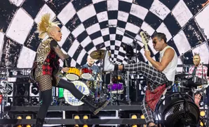 A rock band performs on stage in front of a checkered backdrop.