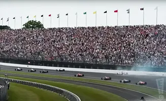 Race cars on track with a full stadium of spectators and flags in the background.