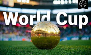 A golden globe trophy sits on the grass of a stadium with a blurry crowd in the background.