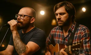 Two men perform music: one sings into a microphone and the other plays an acoustic guitar.