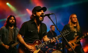 A band performs on stage with colorful lights, the lead singer in a black shirt and baseball cap sings into a microphone.