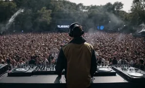 A DJ performs for a large, energetic crowd at an outdoor music festival.