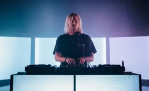 DJ in headphones playing music at a club with a crowd dancing in the background.