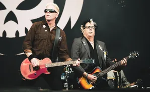 Dexter Holland and Noodles of The Offspring perform on stage with guitars.