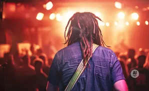 Man with dreadlocks and a denim shirt stands with his back to the camera at a concert.