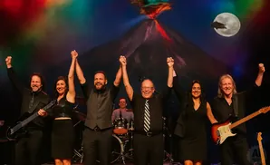 Band on stage with hands raised in front of a volcano backdrop.