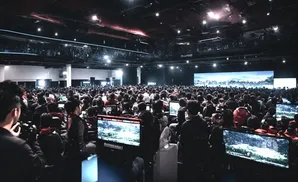 A large crowd watches a screen at an esports event, with gamers at computers in the foreground.