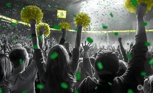 Crowd cheering at a concert, with people holding yellow pom-poms and green confetti falling.