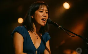 A woman in a blue dress sings into a microphone on stage.