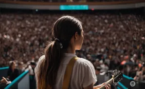Musician playing a guitar on stage in front of a large, cheering crowd.