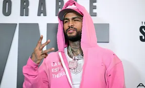 A man in a pink hoodie and cap flashes a peace sign.