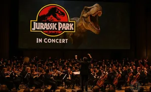 An orchestra performs in front of a large screen displaying the 