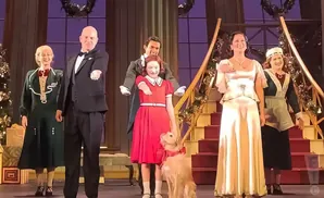 A group of people and a dog on a stage, dressed in festive attire, likely for a holiday performance.