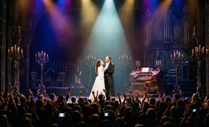 Phantom and Christine embrace on stage with dramatic lighting and candelabras.