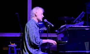Musician playing piano on stage under purple lighting.