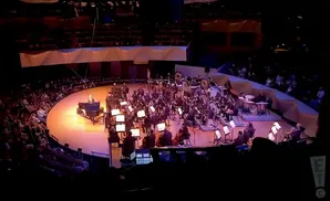 An orchestra performs for a seated audience in a large, circular venue.