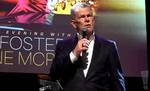 Man in a tuxedo speaks into a microphone on stage, with 