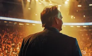 Man in a suit looks out at a brightly lit stadium crowd.