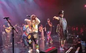 george clinton at the front of the stage with parliament funkadelic behind him.