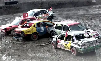 Demolition derby cars are mud-splattered and damaged. A yellow and blue car is center.