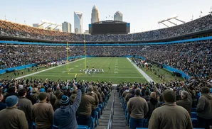 A football game is underway in a packed stadium with a city skyline in the background.