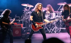 A rock band performs on stage with guitars and drums.