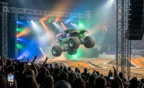 A monster truck, Grave Digger, soars through the air during a show, lit by colorful stage lights.