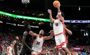 Basketball player in white jersey with number 10 leaps to shoot while guarded by opponent.