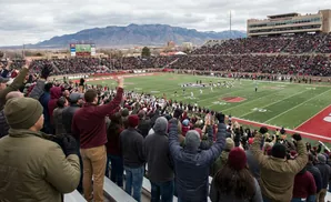 A football stadium full of fans cheering with mountains in the background.