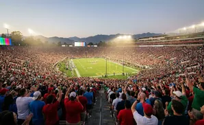 A crowded American football stadium at sunset, with fans cheering on the field.