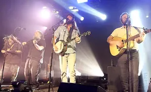A band performs on stage with bright lights and fog.