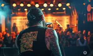 A man with a bun and tattoos sings into a microphone on stage, facing a crowd at a concert.