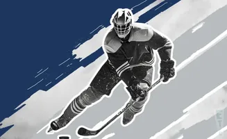 A hockey player in a black and white uniform skates with a puck and stick.