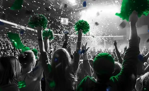 A crowd cheers with green pom-poms and confetti at a concert or sporting event.