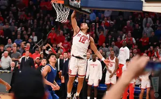 A basketball player in a white #12 jersey dunks the ball as a crowd watches.