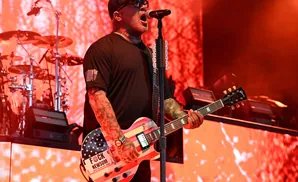 A man in a black t-shirt and baseball cap sings and plays a guitar painted like the American flag.