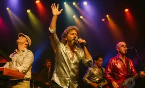 A band performs on stage with colorful lights, a lead singer holds a microphone and raises his hand.