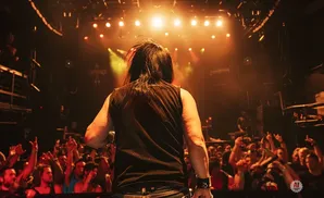 A rock musician with long dark hair performs on stage for an energetic crowd.