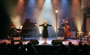 A female singer on stage with a piano and a double bass player, performing for an audience.