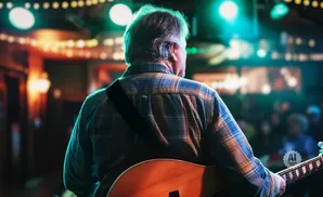 Man playing guitar on stage, lit by blue and yellow lights.
