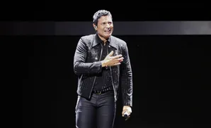 Singer Chayanne smiles and places his hand on his chest on stage, wearing a sparkling black jacket.