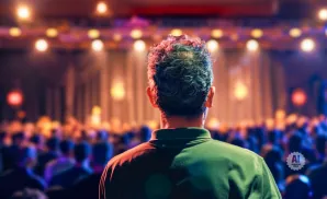 Back of a man's head, facing a blurred audience in a venue with warm lighting.