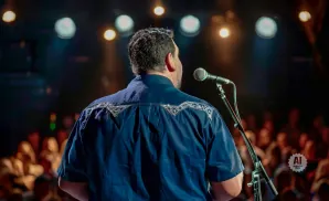 A smiling man with a beard holds a microphone while wearing a black shirt.