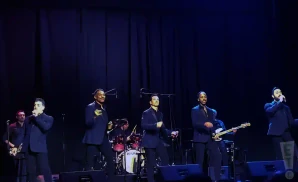 the doo wop project performing on stage in black suits