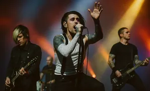 A rock band performs live on stage, with a singer in the foreground and guitarists behind.