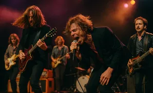 A rock band performs on stage, with a lead singer belting into a microphone and guitarists playing.